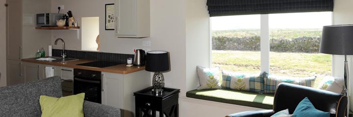 The lounge and kitchen area of the main living space of the Farmhouse accommodation at Castle Stuart Golf links, with views across the course to the art deco styled clubhouse and the Moray Firth.