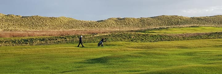 A view of the largely flat links course of Wick Golf Club, with the large grassy sand dunes that separate the course from the sea
